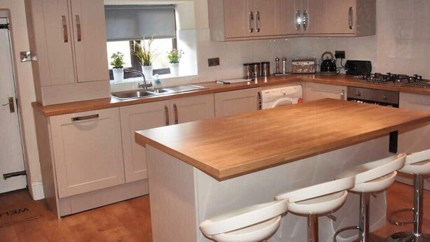 Een moderne keuken met een centraal eiland, barstoelen en lichtkleurige kastjes.