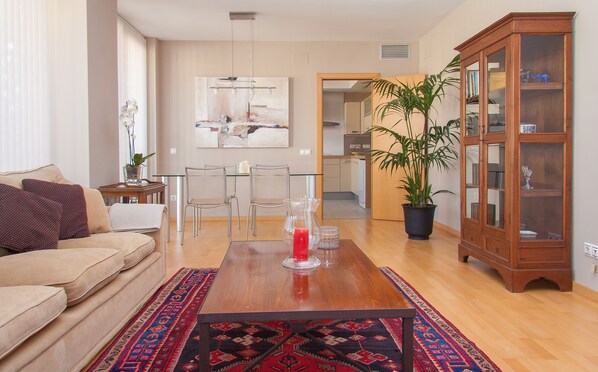 A living room with a sofa, a coffee table, a dining table, chairs, a cabinet, and a potted plant. - Excellent location in the heart of Maresme, 200 meters from the beach (Mataró)