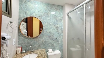 Un baño con salpicadero de mármol, un espejo redondo, un lavabo con grifo, un secador de pelo y un inodoro.