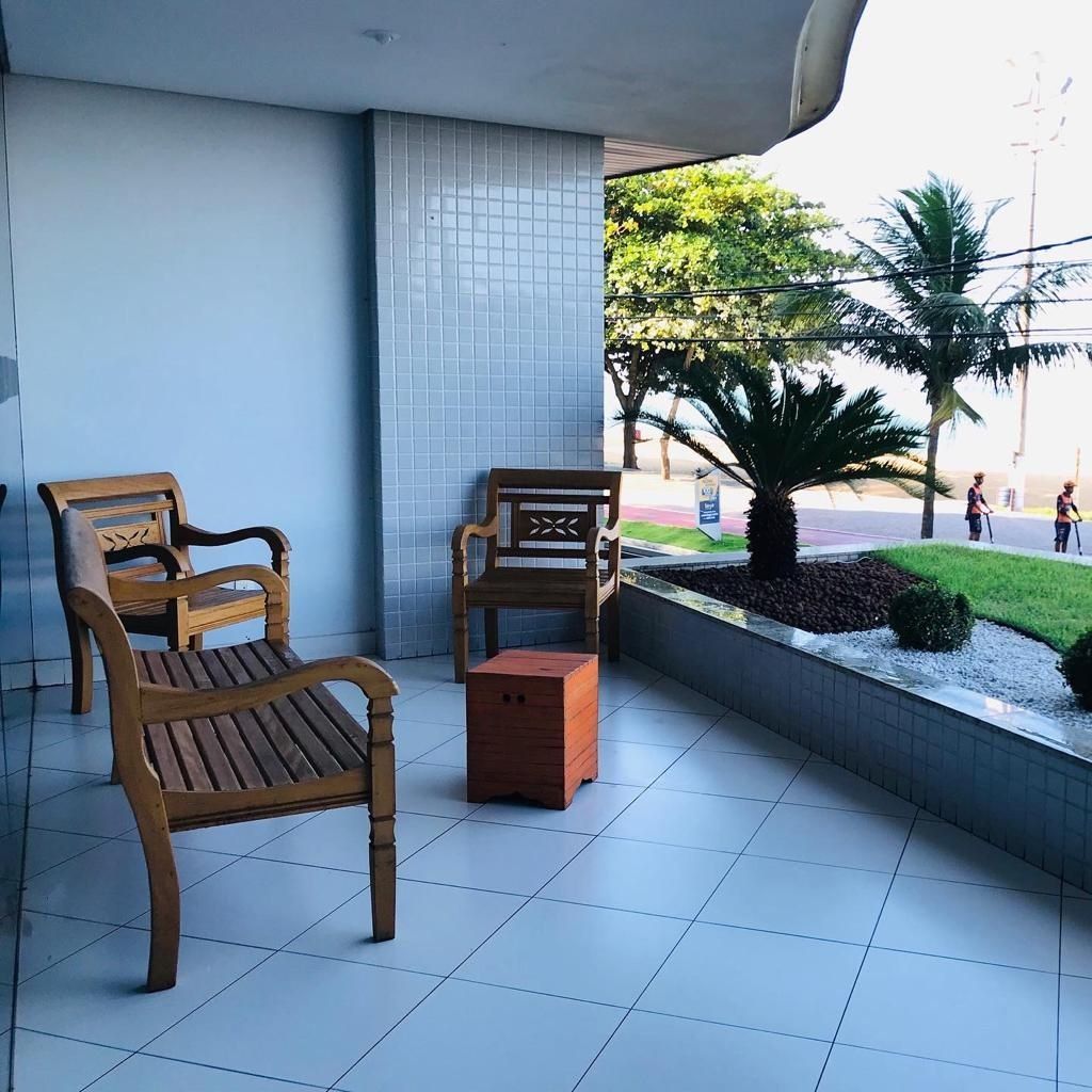 Ein Balkon mit zwei Holzstühlen, einem kleinen Tisch, gefliestem Boden und Blick auf eine Straße mit Palmen und Fußgängern.