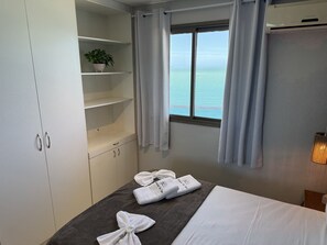 Un dormitorio con cama, ventana con vista al mar, armario y una planta en maceta.