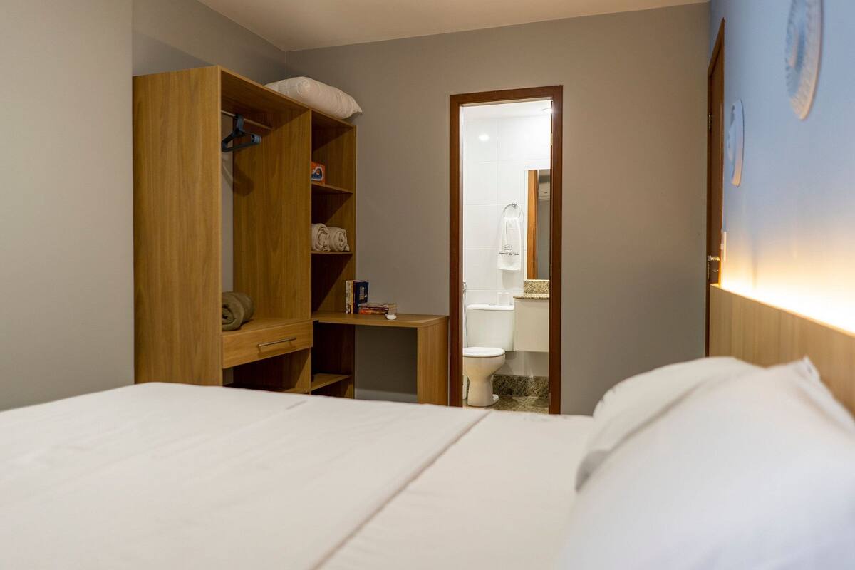 Habitación de hotel con cama, armario de madera y baño visible a través de una puerta abierta.
