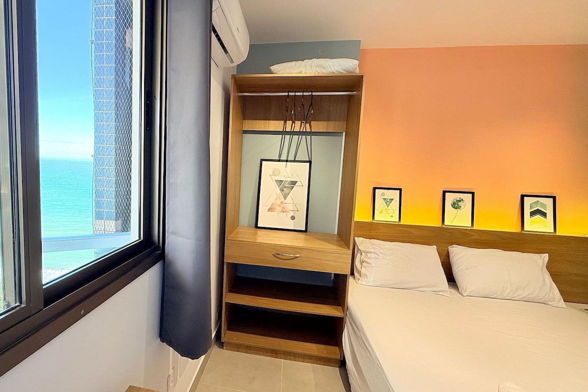 Habitación de hotel con cama, armario, ventana con vista al mar y cuadros en la pared.