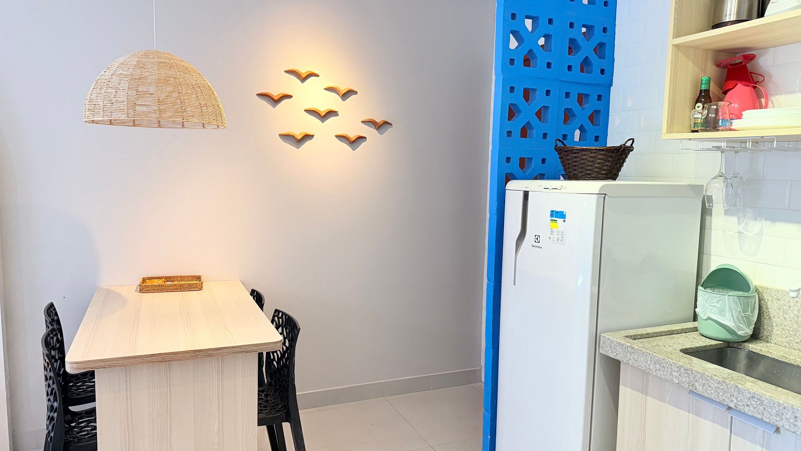 Eine kleine Küche mit einem weißen Kühlschrank, einer gewebten Pendelleuchte und einer blauen Raumtrennung.
