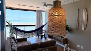 A living room with a hammock, a large hanging light fixture, and a view of the beach. - Diamond Beach (Vila Velha)