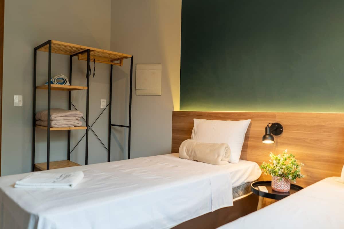 Habitación de hotel con dos camas, un estante de madera, una lámpara de pared y una planta en maceta.