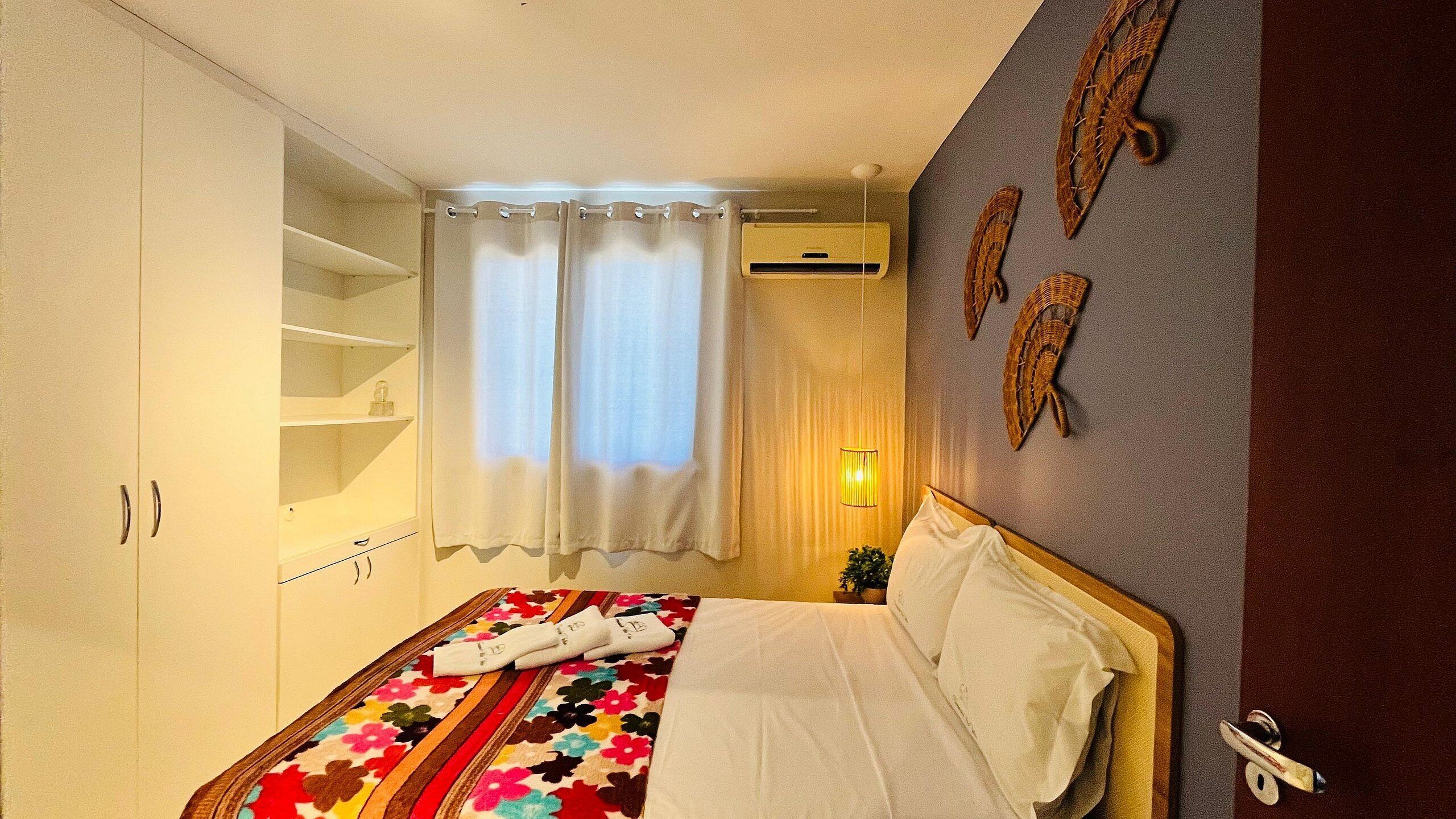 A bedroom with a bed, a wardrobe, a window with curtains, and wall decorations.