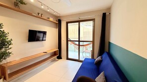 Un salon moderne avec un téléviseur à écran plat fixé au mur, un canapé bleu avec des coussins, un banc en bois et une grande porte-fenêtre coulissante donnant sur un espace extérieur équipé d’un hamac.