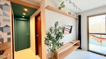 Un pasillo moderno con una puerta verde, un banco de madera, una planta en maceta y un televisor montado.