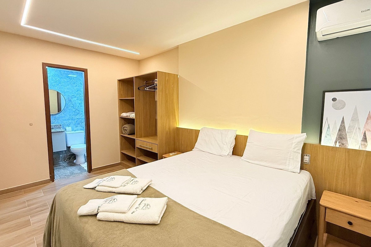 Una habitación de hotel con cama, mesitas de noche, armario y baño visible a través de una puerta abierta.
