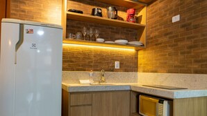 A compact kitchen with a refrigerator, microwave, sink, and shelves above the countertop. - Diamond Beach (Vila Velha)