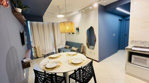 A modern dining area with a round table set for four, a ceiling fan, and a kitchen area with a microwave. - Diamond Beach (Vila Velha)