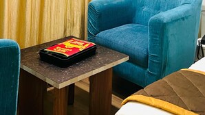 A hotel room with a blue armchair, a small table with a tray, and a curtain. - Hotel Monarch International (Bengaluru)