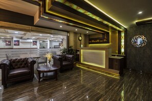 A reception area with leather sofas, a reception desk, and a clock on the wall. - Hotel Monarch International (Bengaluru)