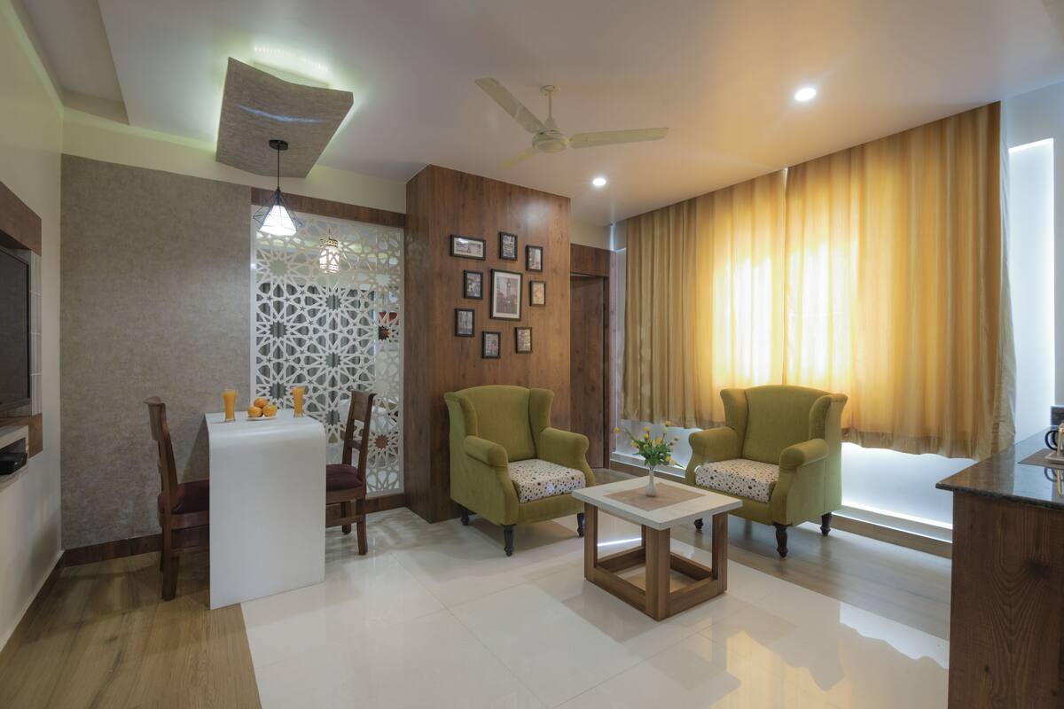 A living room with two green armchairs, a white coffee table, a TV, and a ceiling fan.