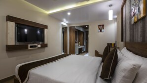 A modern hotel room with a large bed, a flat-screen TV mounted on the wall, a desk with a laptop, and a small painting on the wall. - Hotel Monarch International (Bengaluru)