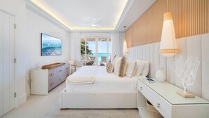 Un dormitori modern amb un llit gran, un escriptori de vidre i vista a l'oceà.