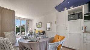 Een eethoek met een ronde tafel voor vier personen, omringd door rieten stoelen, een keuken met witte kastjes en uitzicht op het omliggende landschap.