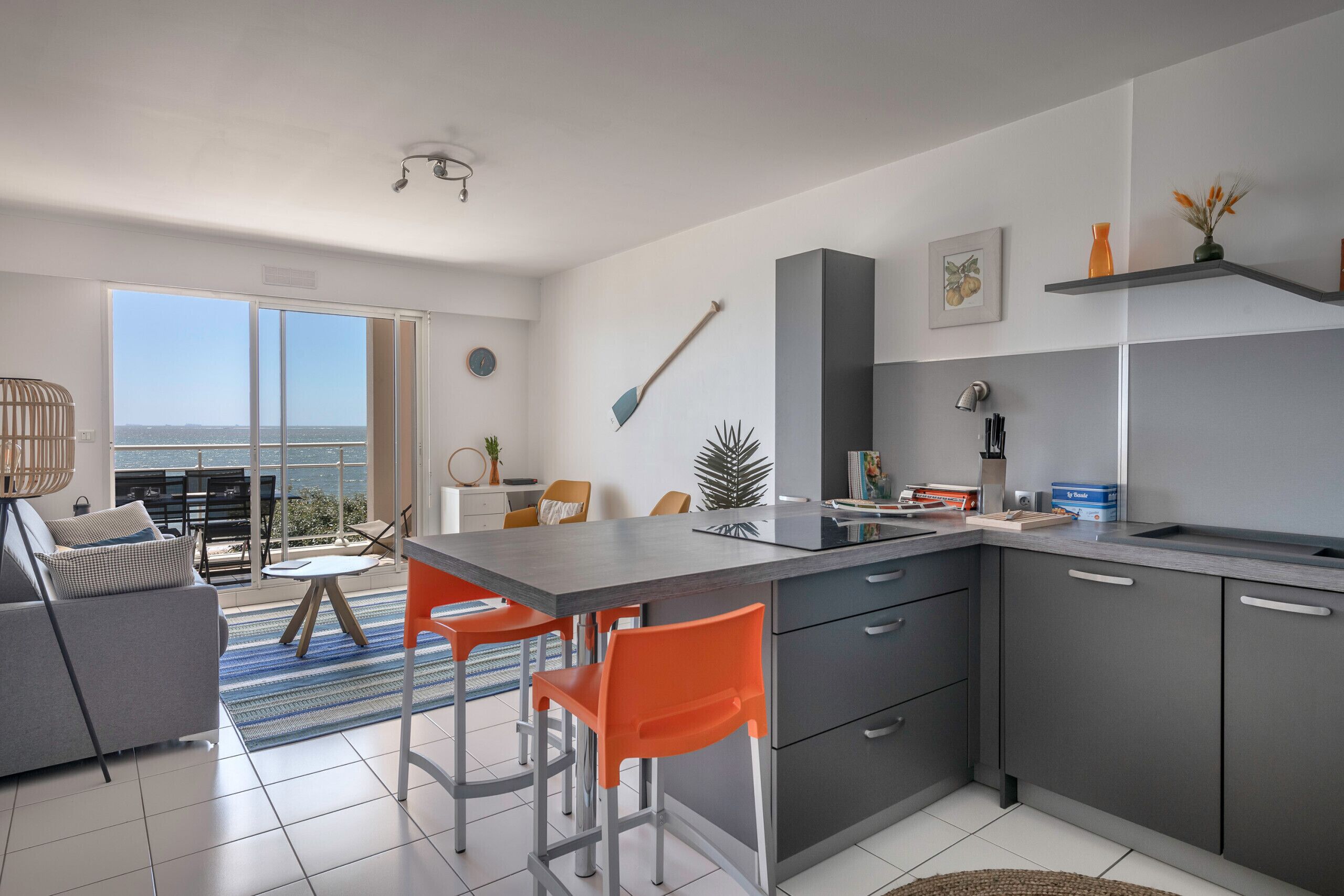 A modern kitchen with a central island, grey cabinets, and orange chairs.