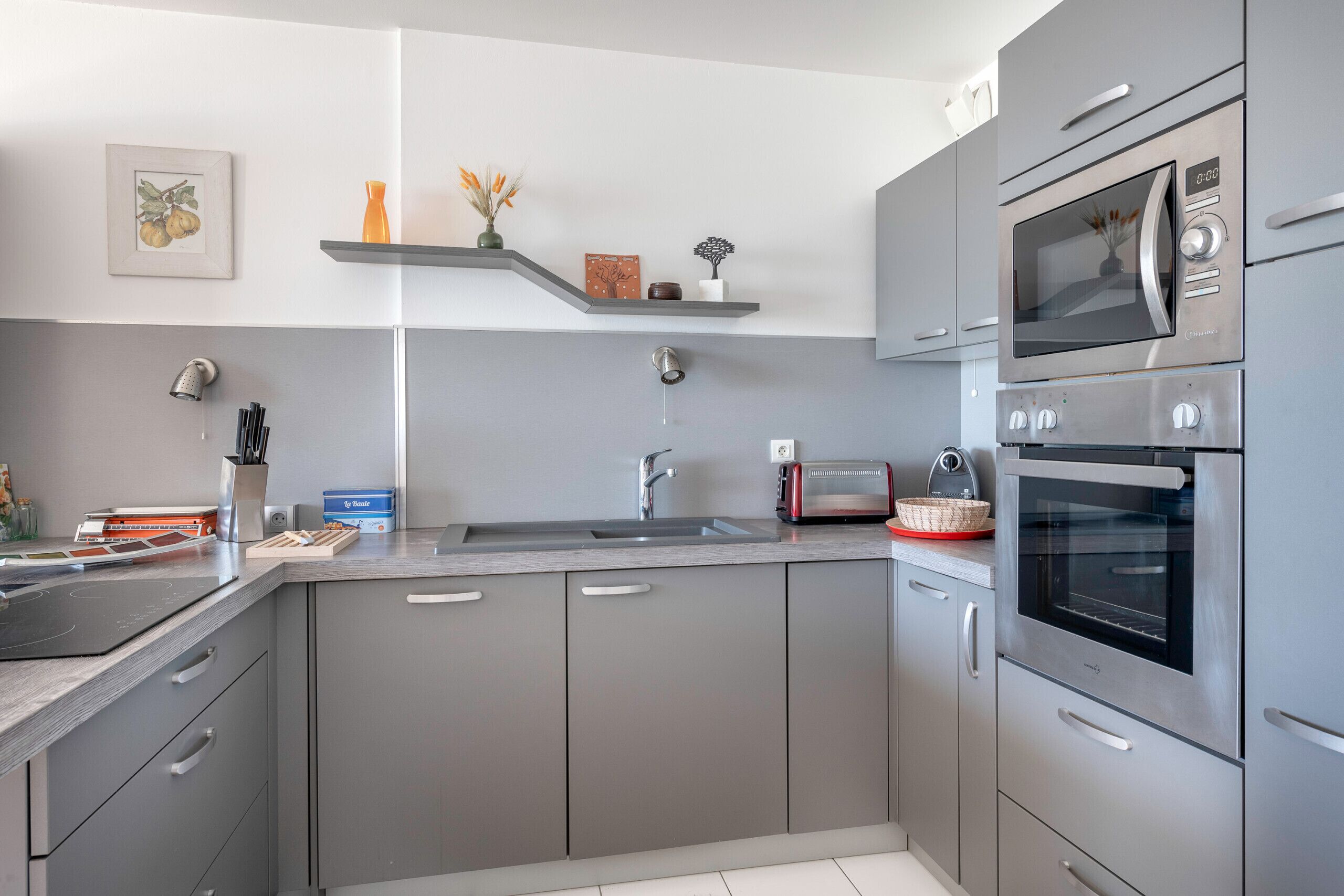 A modern kitchen with grey cabinets, a stainless steel microwave, and a built-in oven.