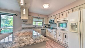 Una cocina con encimeras de granito, armarios blancos, microondas, horno y lavavajillas.