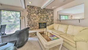 Una sala de estar con pared de piedra, chimenea, sofá color beige y una mesa de centro con revistas.