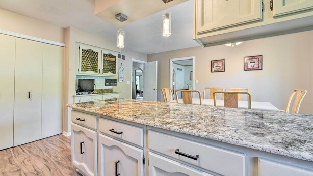 Una cocina con armarios blancos, encimera de granito y zona de comedor con sillas.
