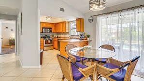A modern kitchen with wooden cabinets, a central island, and a dining area with wicker chairs and a glass table. - Screened Porch & Heated Pool: Cape Coral Home (Cape Coral)