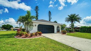 A residential garage with a driveway leading to it, surrounded by well-maintained grass and small flowering plants. - Screened Porch & Heated Pool: Cape Coral Home (Cape Coral)