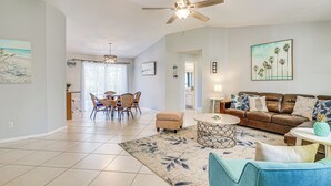 A spacious living room with a ceiling fan, a brown leather sofa, a blue armchair, and a dining area with wicker chairs. - Screened Porch & Heated Pool: Cape Coral Home (Cape Coral)