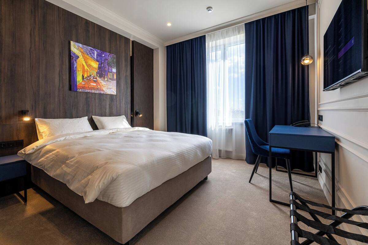 A modern hotel room with a large bed, a desk, and a chair.