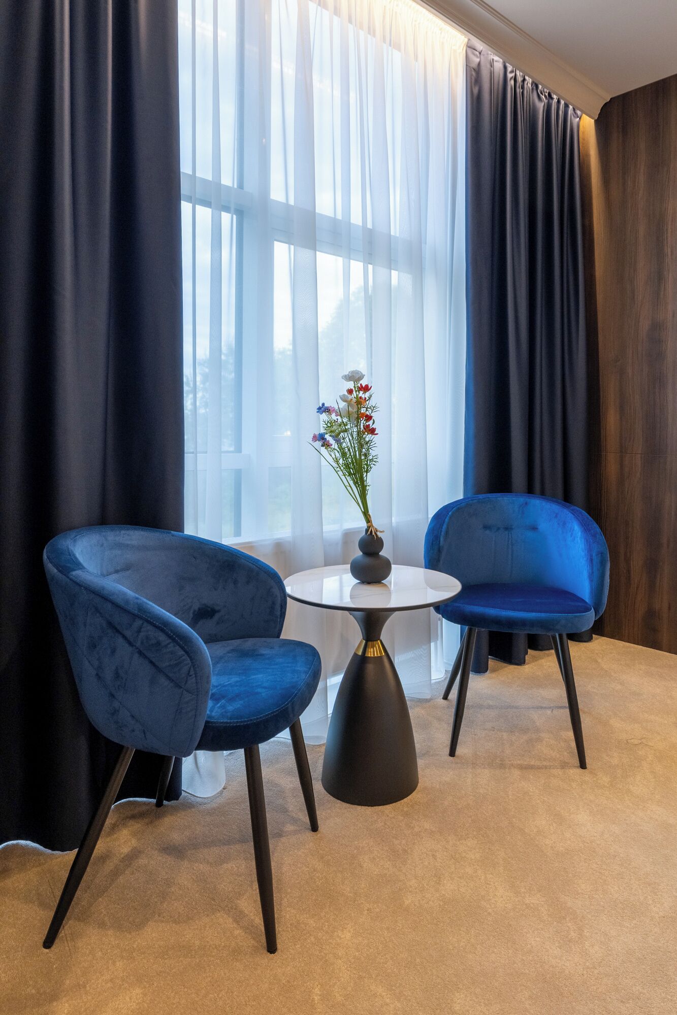 Una habitación con dos sillas azules, una mesita redonda y un florero con flores.