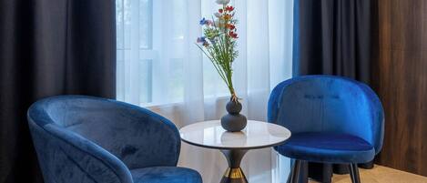 Una habitación con dos sillas azules, una mesita redonda y un florero con flores.
