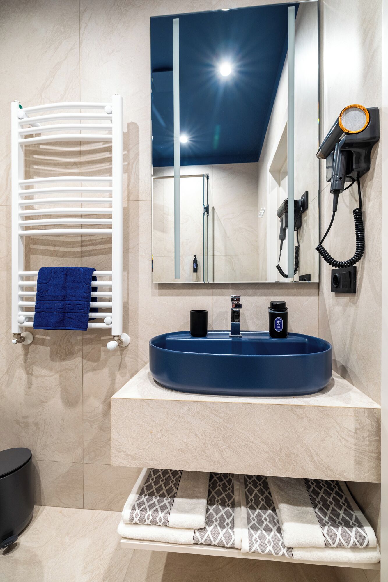 Un baño moderno con un lavabo redondo azul, un toallero blanco y un secador de pelo fijado a la pared.