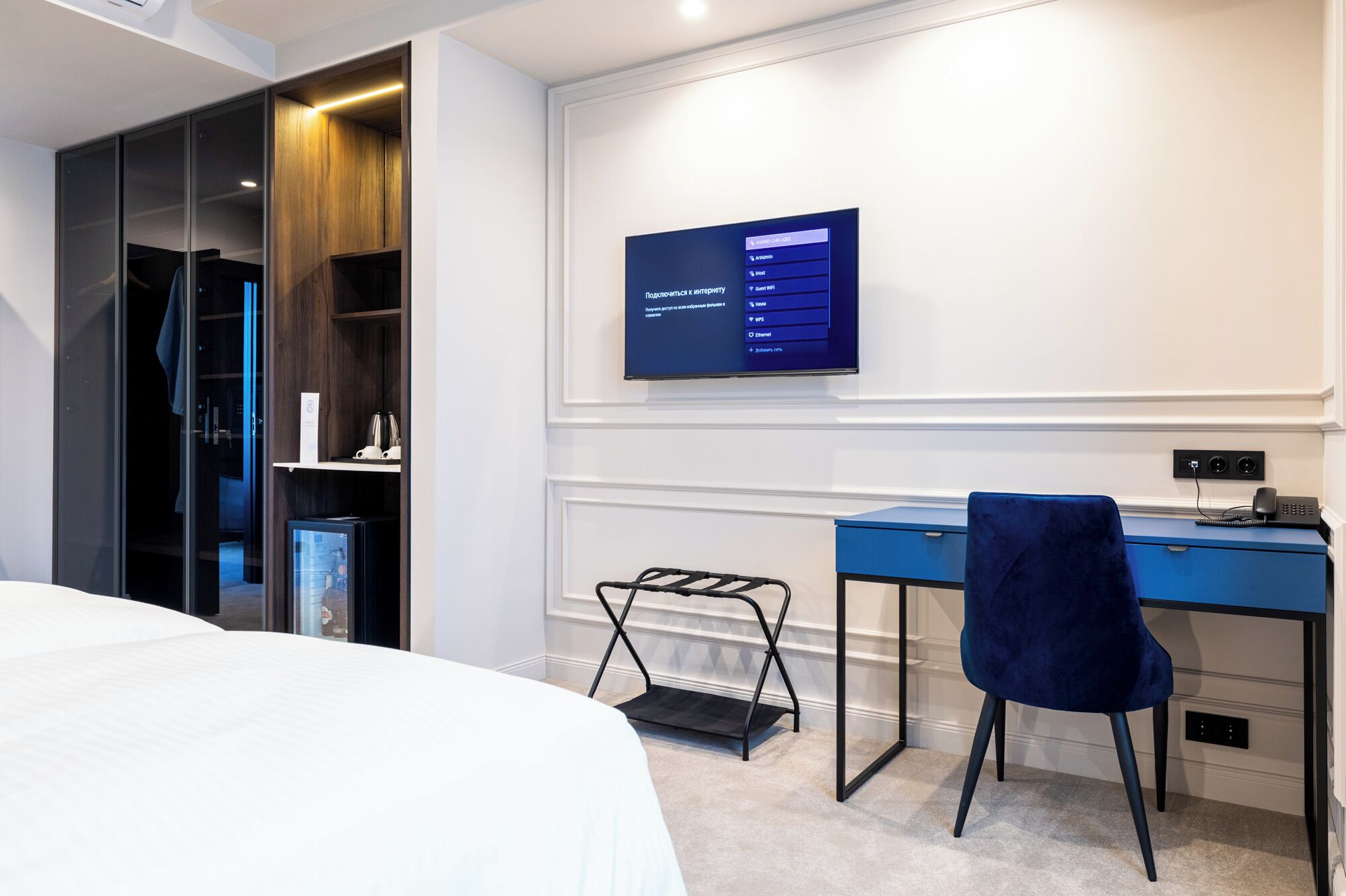 Una habitación de hotel moderna con una cama, un escritorio, una silla y un televisor mostrando un menú.