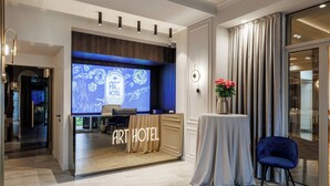 A hotel lobby with a reception desk, a seating area, and a large screen displaying the hotel name. - Art Hotel (Chisinau)