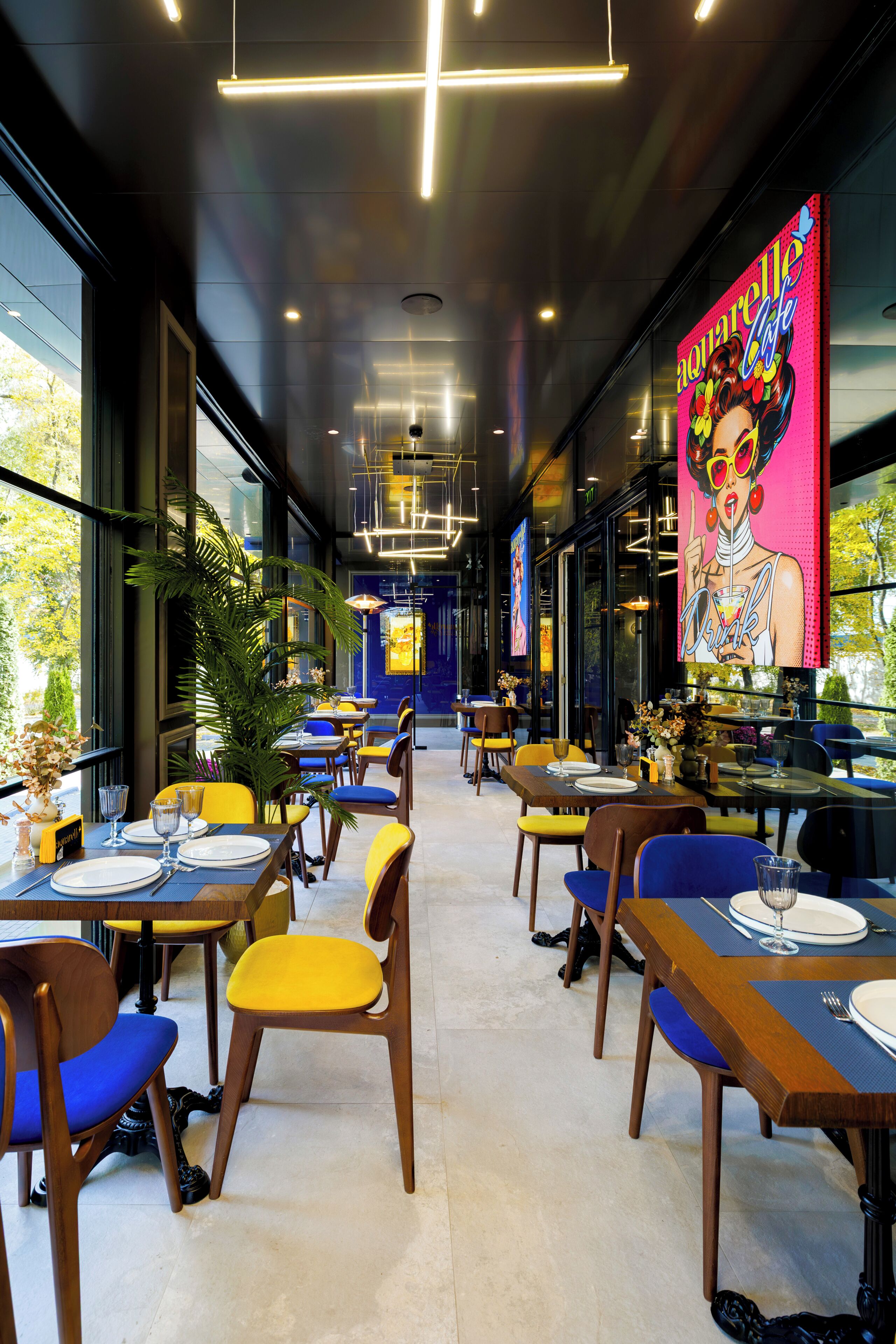 A modern restaurant interior with tables, chairs, and a large digital advertisement on the wall.
