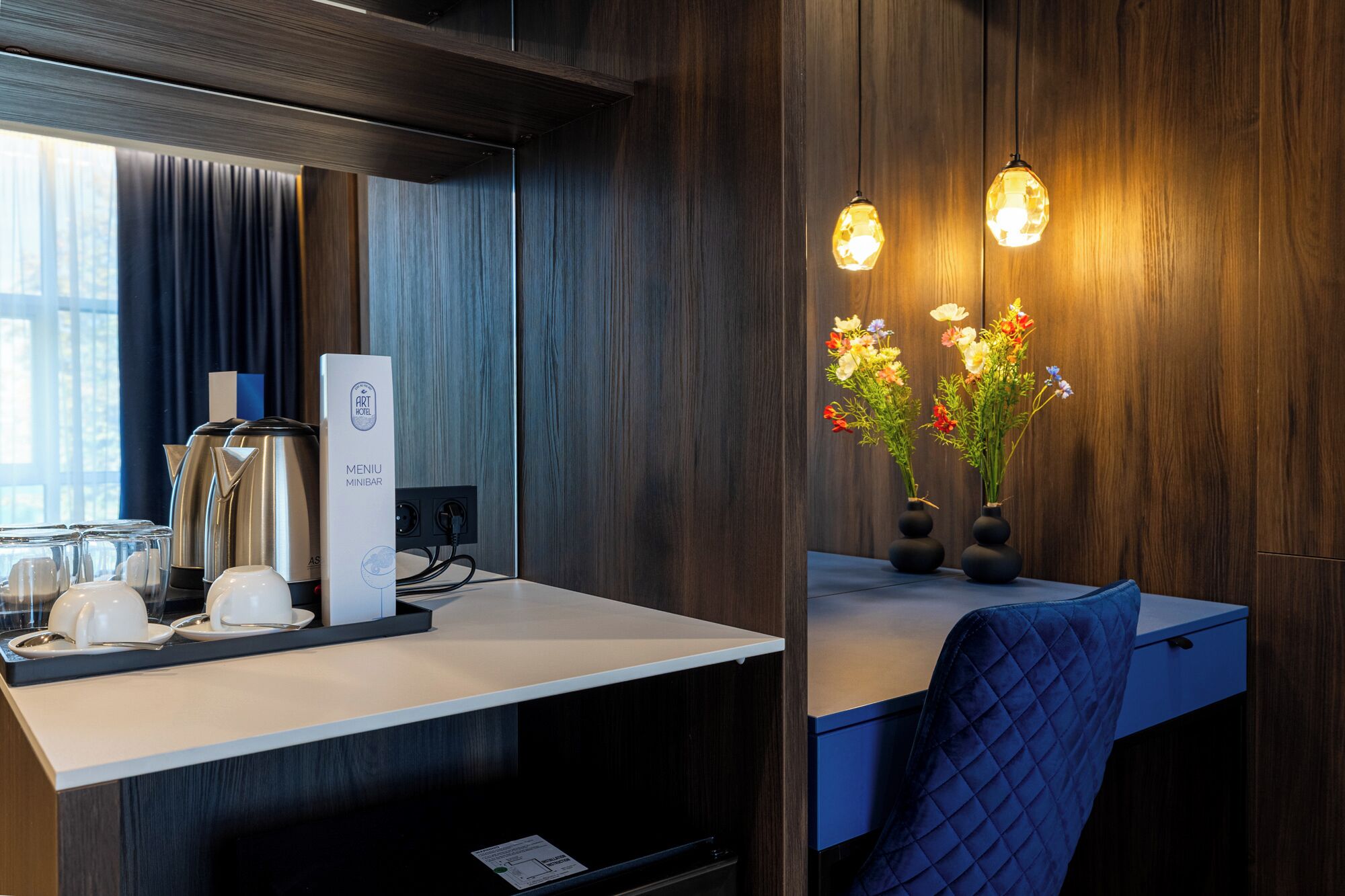 Ein Hotelzimmer mit Holzwand, einem Schreibtisch mit Computer, einer Kaffeemaschine und einer Vase mit Blumen.