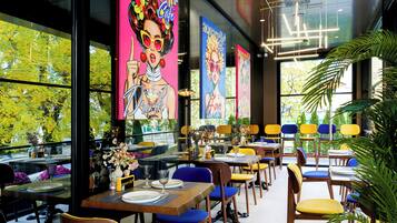 A restaurant with multiple tables and chairs, large windows, and a ceiling with exposed lighting fixtures.
