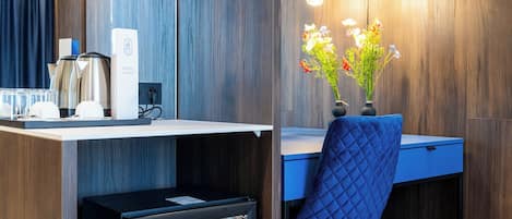 A compact workspace with a desk, a chair, a minibar, and a hanging light fixture.