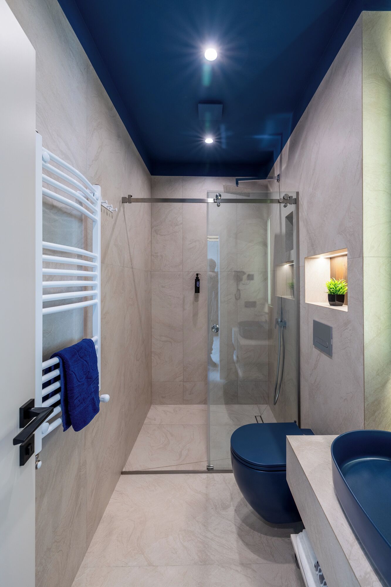 A modern bathroom with a glass-enclosed shower, a white towel rack with a blue towel, and a large blue basin.