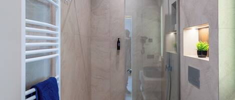 A modern bathroom with a glass-enclosed shower, a white towel rack with a blue towel, and a large blue basin.