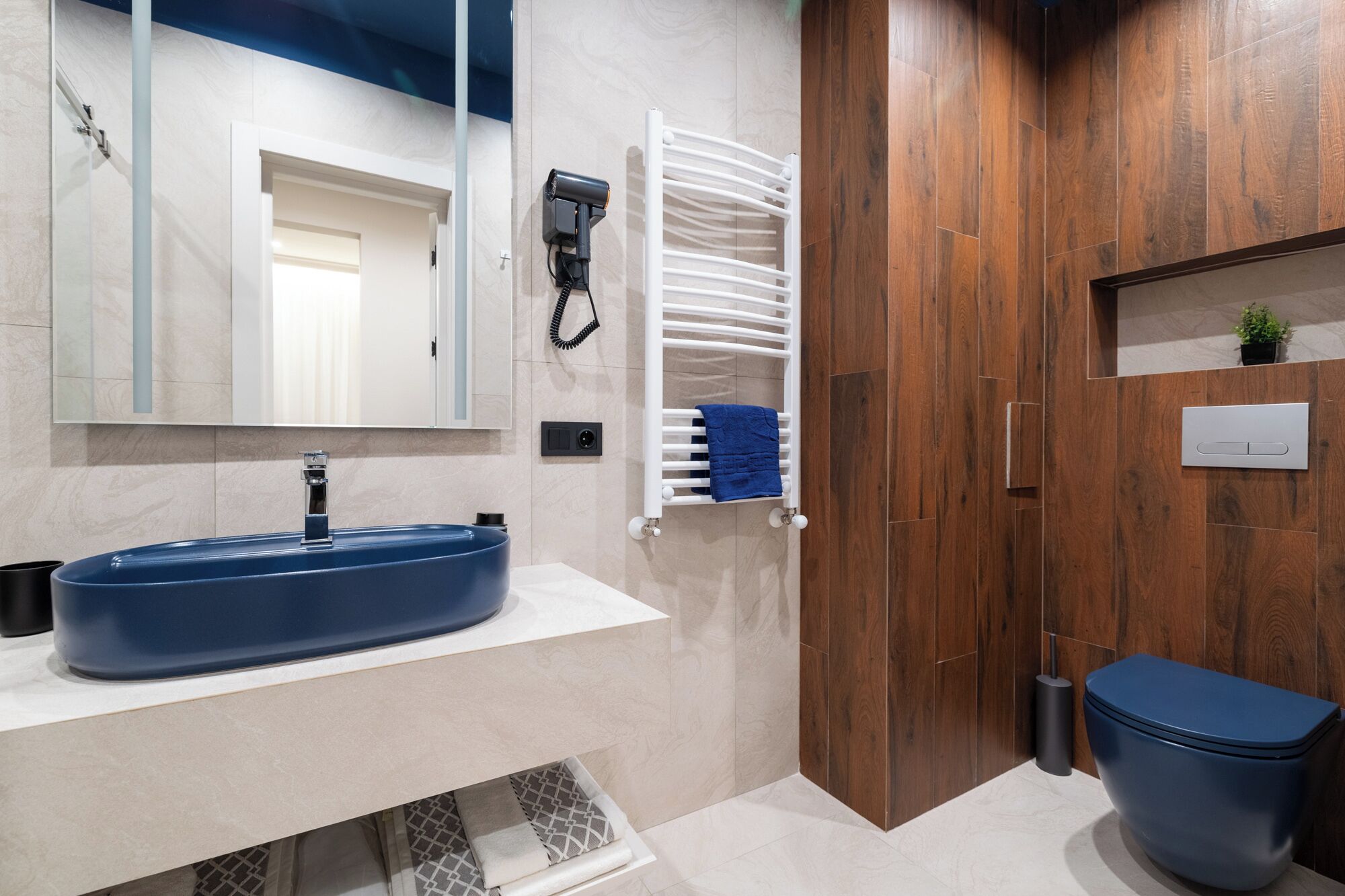A modern bathroom with a blue sink, a white towel rack, and a wooden door.