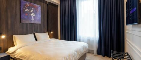 A hotel room with a large bed, a painting on the wall, a TV, and a window with curtains.
