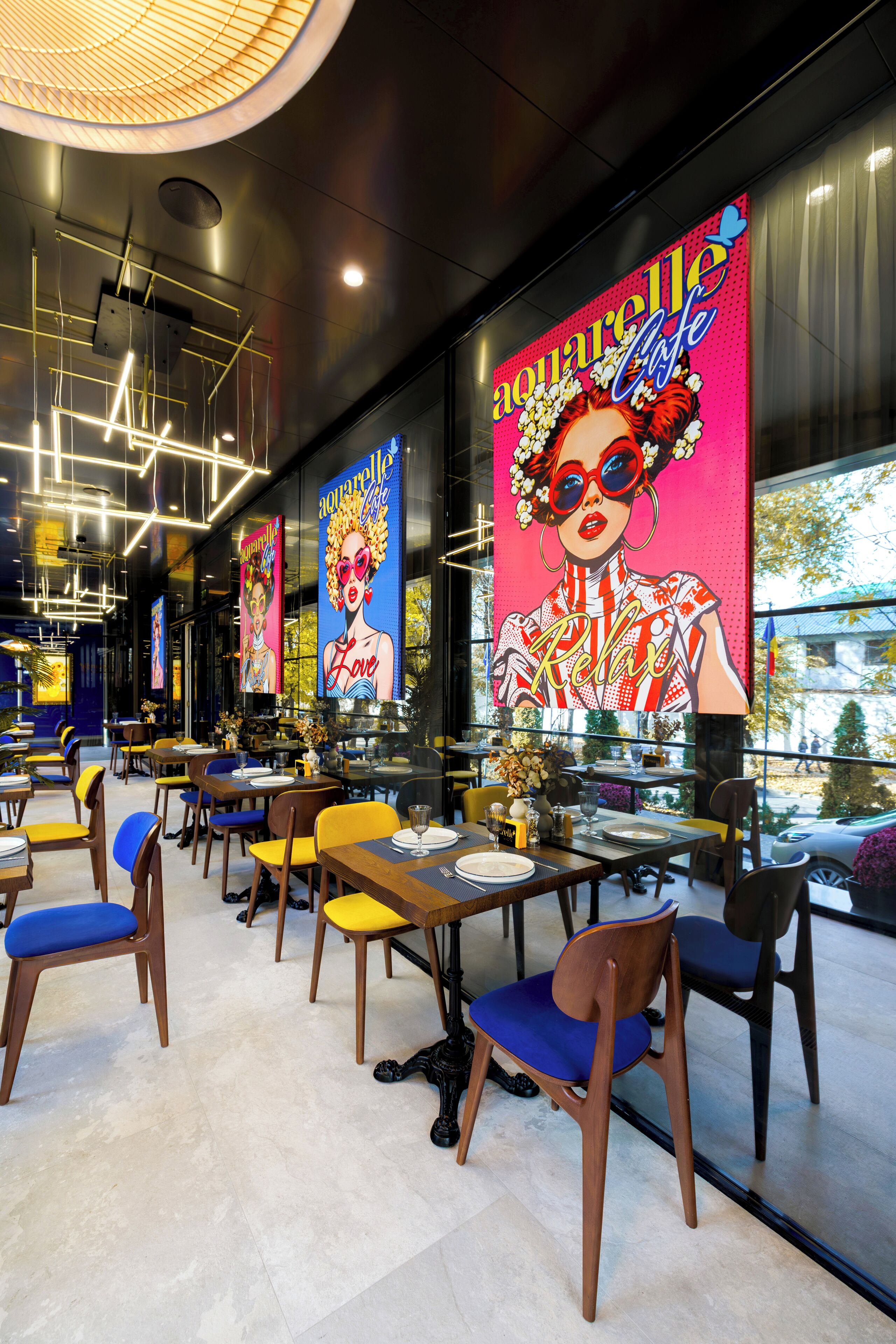 A modern restaurant interior with tables, chairs, and large colorful posters on the walls.
