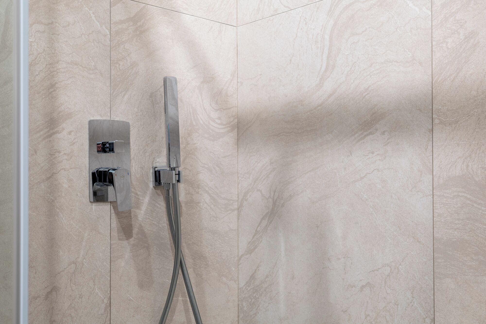 A shower with a control panel and a handheld showerhead against a textured wall.