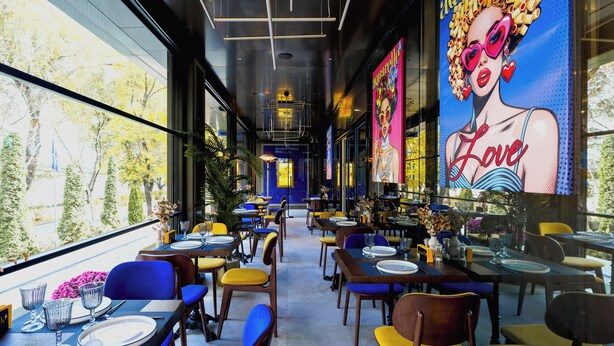 A restaurant with tables set for dining, chairs, and a large mural on the wall. - Art Hotel (Chisinau)