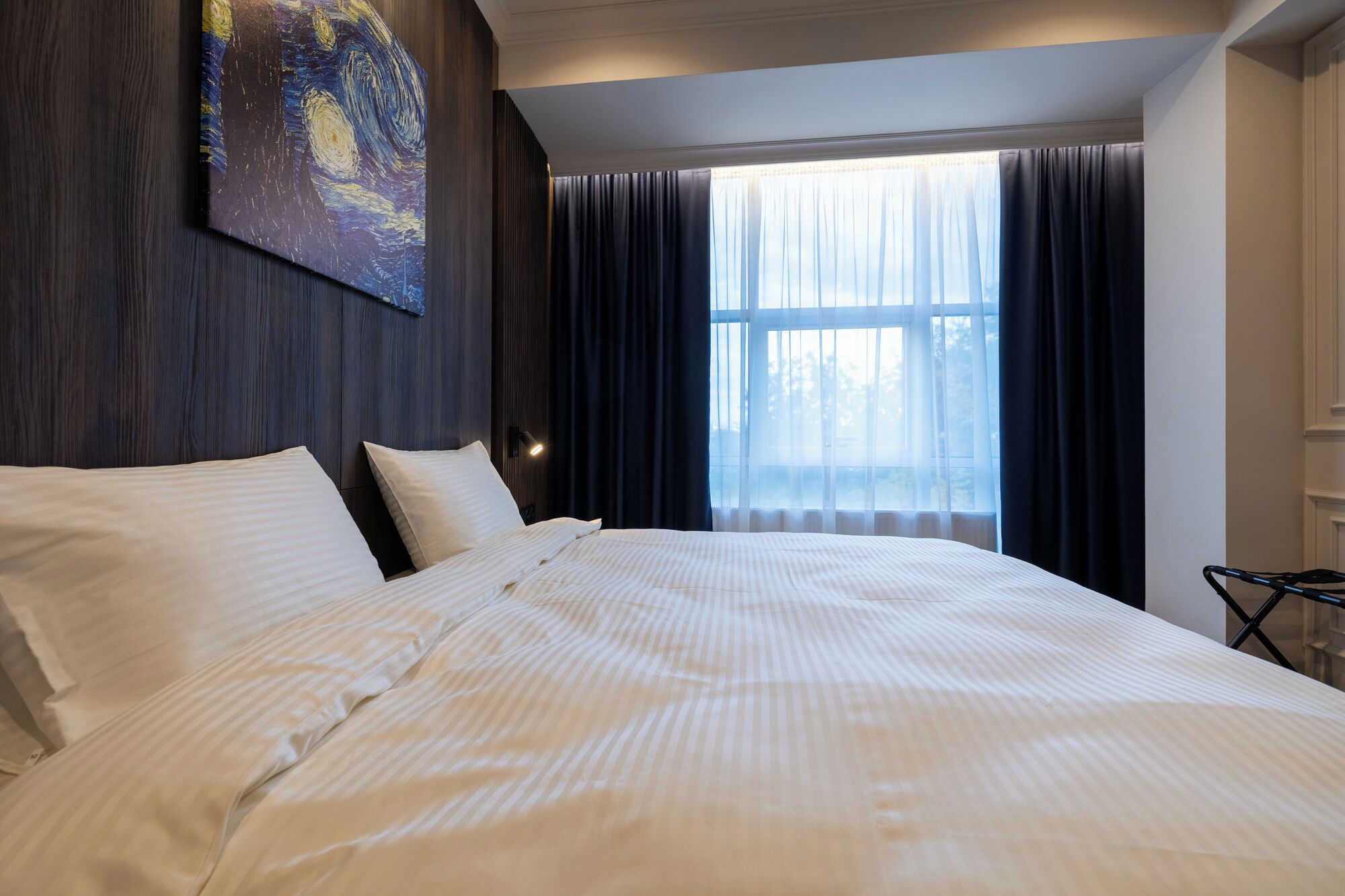Une chambre d’hôtel avec un grand lit, un tableau au mur et une fenêtre avec des rideaux.
