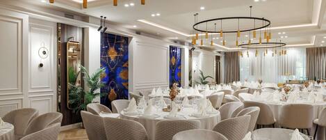 Un salón de banquetes con mesas redondas dispuestas para comer, con sillas blancas y vajilla.