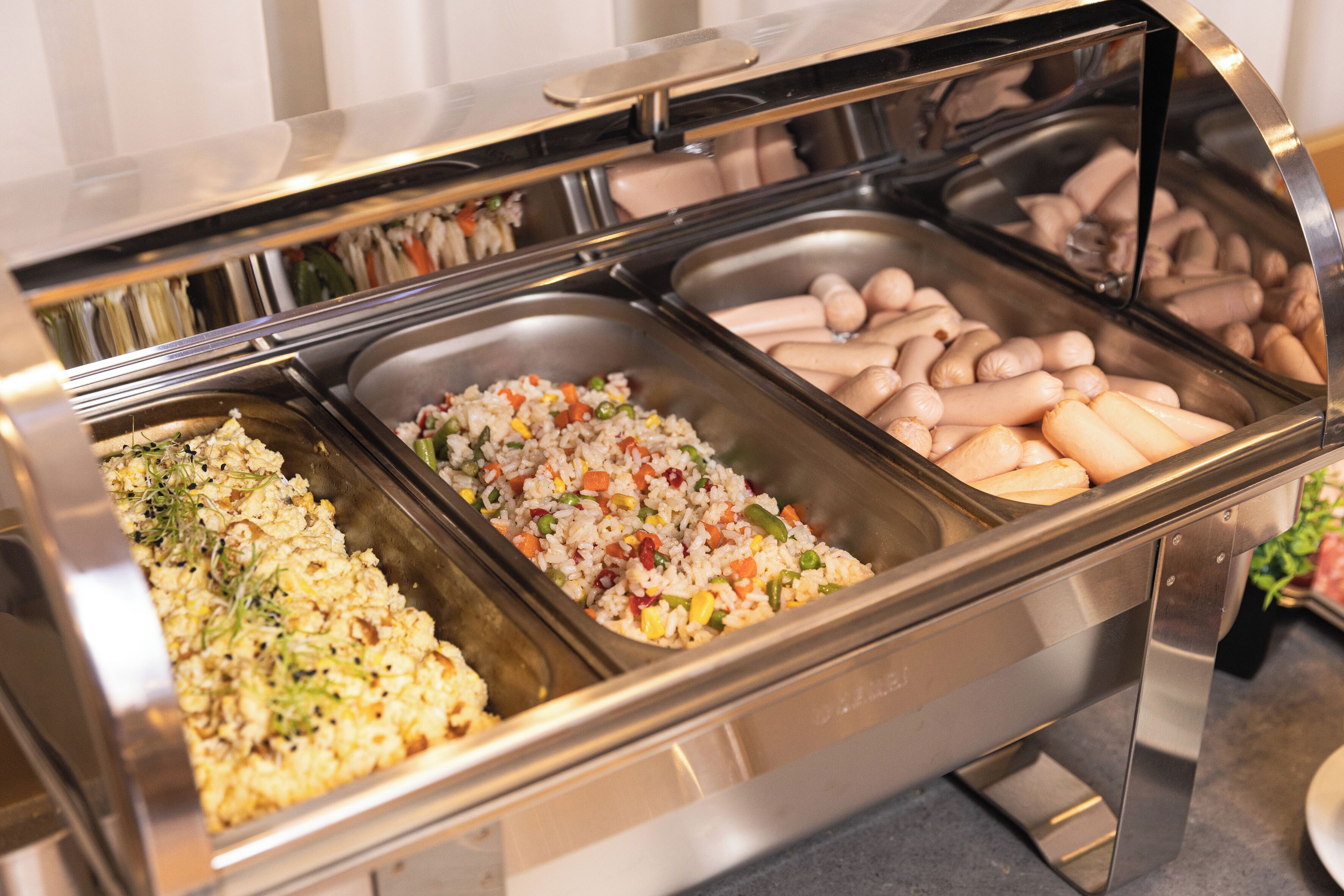 Un bufé con diversas opciones de comida, incluyendo platos de arroz, salchichas y otras preparaciones.